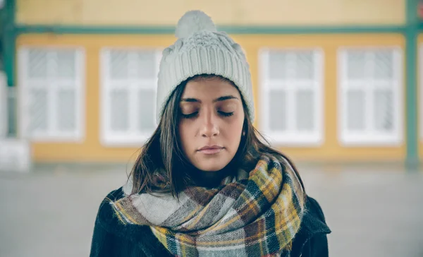 Young girl with closed eyes wearing hat and scarf