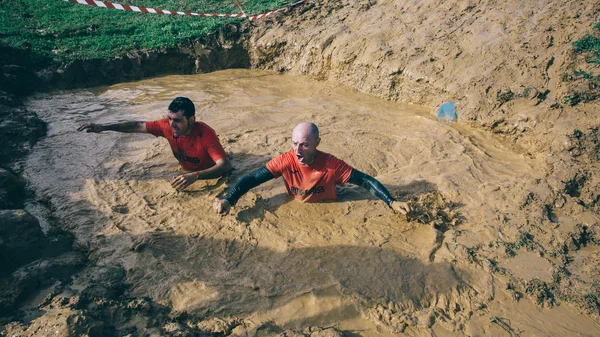 Бегуны пересекают грязевую яму в экстремальной гонке препятствий — стоковое фото