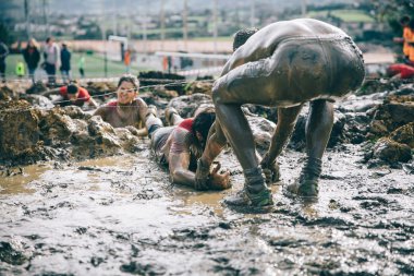 Runner helping woman to crawling under barbed wire in a test of extreme obstacle race
