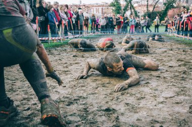 Runner crawling under electrified mesh in a test of extreme obstacle race