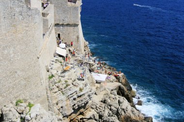 insanlar Dubrovnik'in eski şehir merkezinde Adriyatik Denizi kıyısına yakın küçük kayalık duvar sahilde rahatlatıcı