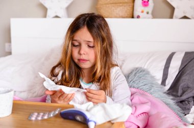 Küçük kız hasta, üşütmüş ve üzgün. Yatak odasındaki yatakta haplı ve termometresi olan çocuk. Viral hastalık konsepti ve covid 19.
