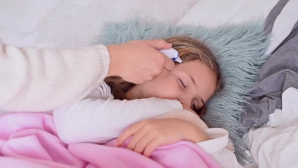 Una bambina dorme a letto, ha il raffreddore, è malata. La mamma sveglia il bambino e misura la temperatura con un termometro elettronico. Concetto di cura della malattia virale — Video Stock