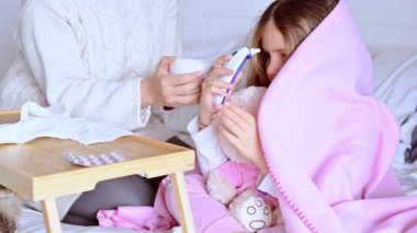 Küçük bir kız yatakta uyuyor, üşütmüş, hasta. Anne bebeği uyandırır ve ısıyı elektronik termometreyle ölçer. Viral Hastalık Bakımı Konsepti