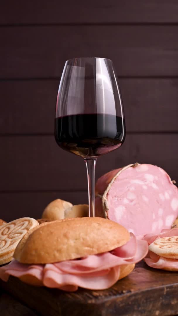 Een glas rode wijn, mortadela, tijel en verschillende broden op een houten tafel. Een traditionele pre-diner starter in de Noord-Italiaanse regio Emilia Romagna. Verticale video voor smartphones. — Stockvideo