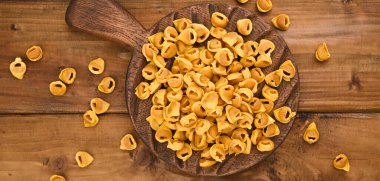 Tortellini mignon ahşap bir tahtada fesleğen ve parmesanlı. Bologna ve Emilia Romagna mutfağının spesiyaliteleri: Cappelletti, et ve sebzeli taze yumurtalı makarna..