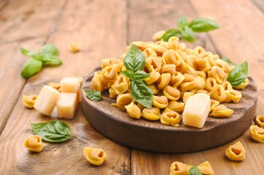 Tortellini mignon ahşap bir tahtada fesleğen ve parmesanlı. Bologna ve Emilia Romagna mutfağının spesiyaliteleri: Cappelletti, et ve sebzeli taze yumurtalı makarna..