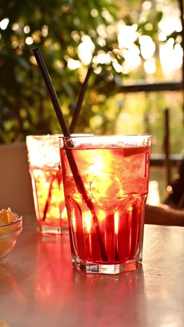 Aperol injekční stříkačka ve sklenici na stole v restauraci. Letní kavárna v italském parku. Sluneční paprsky v rámu. Svislé video. — Stock video