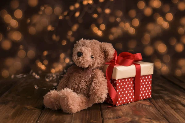 Urso de pelúcia e caixa de presente com arco. Presente de Natal e luz de guirlandas com bokeh de ouro no fundo. Foto em estilo retro. — Fotografia de Stock