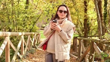 Çevre koruma programında maskeli ve kahveli bir kız sonbahar parkında dinleniyor. Dışarıda kahvesi olan genç bir kadın..