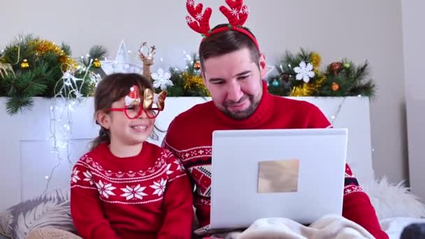 Uma filha de chapéu de Natal e pai estão parabenizando por uma videochamada Feliz Natal e Ano Novo. Férias online de Natal em 2021. Família feliz com laptop para comunicação. — Vídeo de Stock