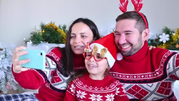 Szczęśliwa rodzina w święta rozmawia przez wideo komunikacji w Boże Narodzenie. Mama, tata i córeczka dobrze się bawią. Świętowanie nowego roku w domu w 2021. online — Wideo stockowe