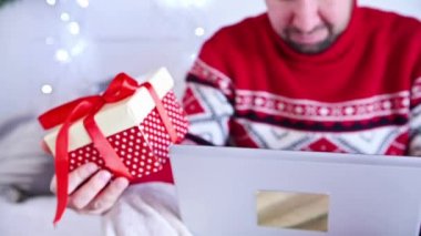 Kırmızı Noel kazağı giyen bir adam evden sürpriz internet siparişi veriyor. İnternetten noel hediyesi almak - online alışveriş konsepti. Yeni yıl tatili konsepti. Dikey video. 4k görüntü