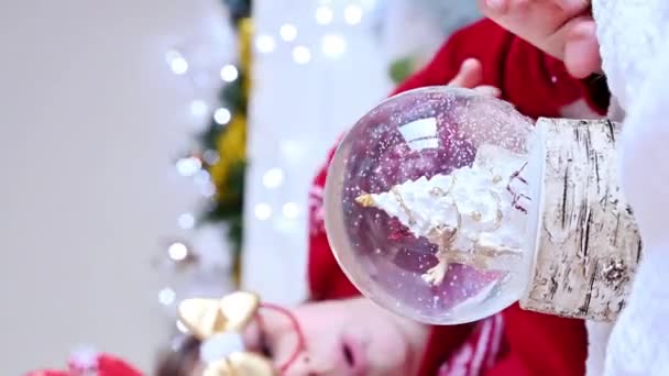 Κοριτσάκι που παίζει με χριστουγεννιάτικη μπάλα σε ένα όμορφο σπίτι με γιορτινή διακόσμηση. Κάθετο βίντεο για το sartphone. — Αρχείο Βίντεο