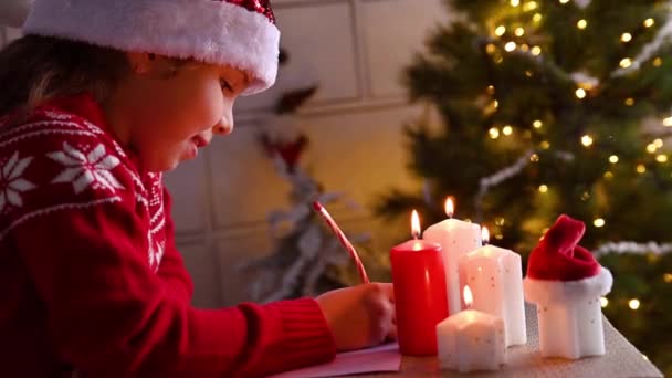 Kleines Mädchen schreibt einen Brief an den Weihnachtsmann in einem süßen, weihnachtlich dekorierten Haus. Das Kind träumt von Teenagern für das neue Jahr. Hochwertiges 4k Filmmaterial