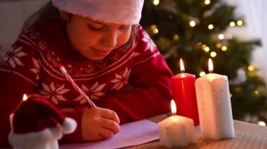 Noel için dekore edilmiş güzel bir evde Noel Baba 'ya mektup yazan küçük bir kız..
