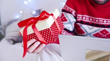 Kırmızı Noel kazağı giyen bir adam evden sürpriz internet siparişi veriyor. İnternetten noel hediyesi almak - online alışveriş konsepti. Yeni yıl tatili konsepti. Dikey video. 4k görüntü