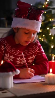 Noel için dekore edilmiş güzel bir evde Noel Baba 'ya mektup yazan küçük bir kız..