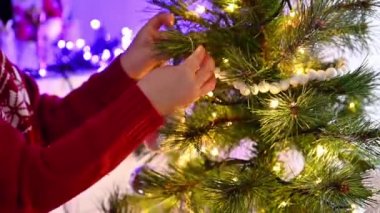 Noel Baba şapkalı küçük bir kız rahat bir evde Noel ağacını süslüyor. Noel ve Yeni Yıl kutlamaları için hazırlıklar.