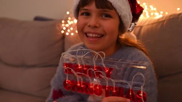 El niño sonríe y sostiene una guirnalda con el texto en letras inglesas - María Navidad. Niña en una habitación decorada para Navidad. — Vídeo de stock