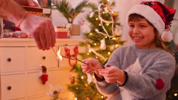 Little girl with sparklers in her hands. Dad lights the Christmas lights for the baby. Happy winter holidays at home. — Stock Video