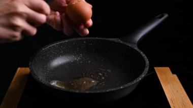 Kızartma tavasında yumurta. Bir kadın kahvaltı hazırlar, yumurtayı bastırarak kırar..