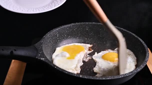 Uova fritte in una padella con burro. Uova per una colazione tradizionale. La donna mette l'uovo su un piatto — Video Stock