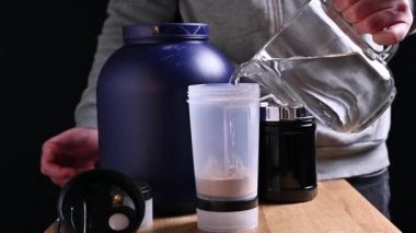 Adam besin takviyeleriyle spor kokteyli yapıyor. Masada beyaz protein ambalajı var. Fitness, vücut geliştirme, sağlıklı yaşam tarzı konsepti. 