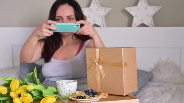 Young Woman fotografeert haar verrassing voor sociale netwerken. Ontbijt op bed en een boeket bloemen voor uw geliefde vrouw. Vrouwendag vakantie concept. — Stockvideo