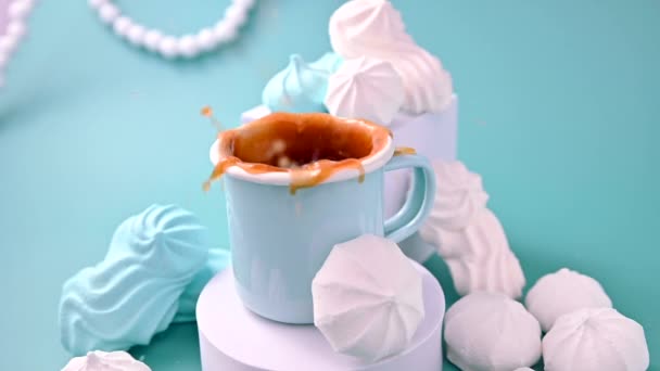 Figurka s meringue spadne do šálku černé kávy a šplouchne mouchou. Espresso s pěnou a meringues různých barev na modrém pozadí. Kreativní záběr bílkovin a cukrových sušenek — Stock video