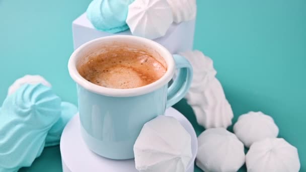 Una meringa e un caffè. Espresso con schiuma e meringhe di diversi colori su sfondo blu. Rallentatore. — Video Stock