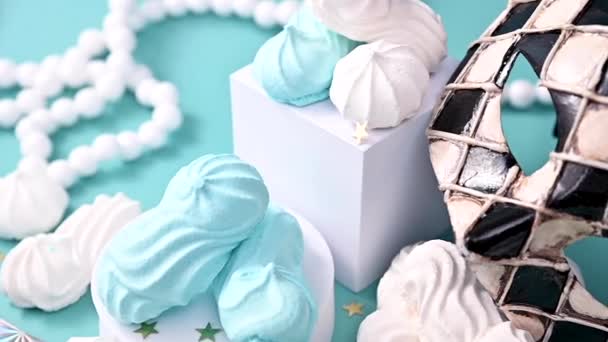 ベネチアンカーニバルとブルーの背景に多色のメレンゲ。イタリアのお菓子で休暇のための伝統的なマスク。創造的な写真。テキストのためのフリースペース. — ストック動画