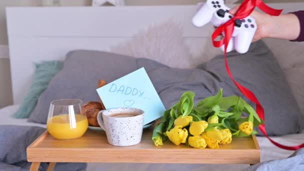 Um presente para um homem, uma consola de computador. Pais surpresa dia para o pai, café da manhã romântico e jogo de computador. Mulher abre uma caixa com um presente — Vídeo de Stock