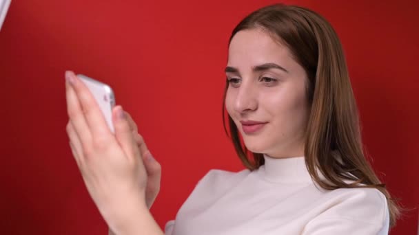 A young girl holds a phone in her hands. Filming on a red background in the studio. Smartphone communication and modern technology. — Stock Video