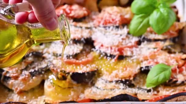 Olijfolie wordt in lasagne gegoten. Traditioneel Italiaans eten. Gebakken aubergine, tomaten met saus, parmezaanse kaas en basilicum. Rustiek voedsel voor een gezond dieet. Groenten voor de lunch. — Stockvideo