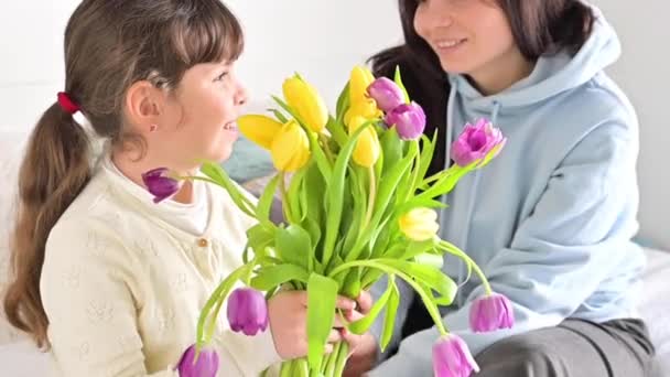 Una bambina regala un bouquet di tulipani gialli e viola a sua madre. Abbracci amorevoli affettuosi di figlia e mamma durante la festa della mamma. Regalo per l '8 marzo per mamma. — Video Stock