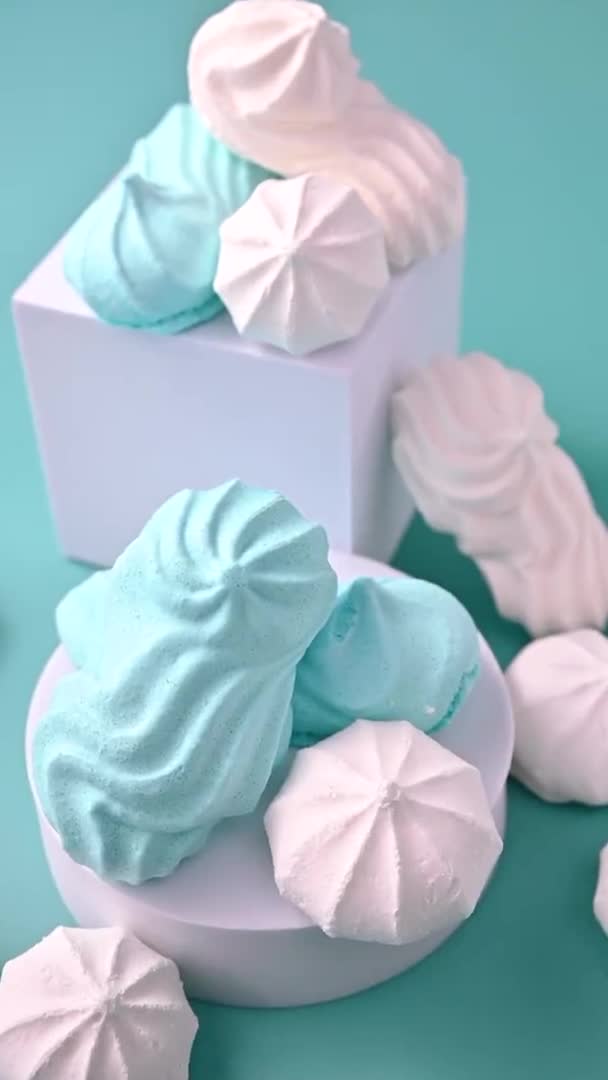 Figures of meringue of different colors on a blue background. Traditional Italian sweets made from proteins and sugar. Videos in bright light colors. Light meringue cookies. vertical,slow-motion. — Stock Video