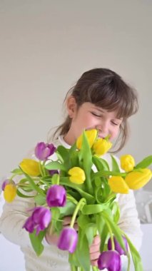 Elinde parlak lalelerden oluşan bir buket olan küçük bir kız, 8 Mart 'ta ya da Anneler Günü' nde bunları annesine veriyor. Annem ya da büyükannem için bir hediye. Bahar çiçeği buketi. Dikey 