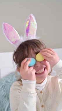 Tavşan kulaklı küçük mutlu kız renkli Paskalya yumurtalarıyla oynayarak eğleniyor. Bir çocuğun ellerinde paskalya için farklı renkte çikolatalar..
