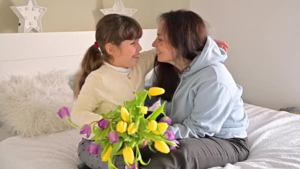 O fetiță dă un buchet de lalele galbene și violet mamei ei. Îmbrățișări iubitoare afectuoase ale fiicei și mamei în ziua mamei. Cadou pentru 8 martie pentru mami . — Videoclip de stoc