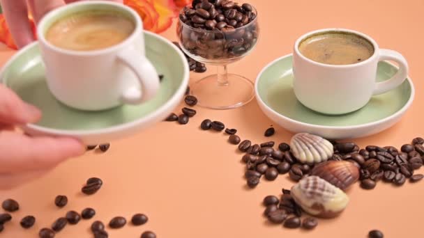 Kawa espresso w ręku. Aromatyczna włoska kawa z piękną śmietaną. Arabica ziarna kawy do produkcji tradycyjnego napoju i bukiet róż na tle. Kobiece ręce w kadrze. materiał filmowy — Wideo stockowe