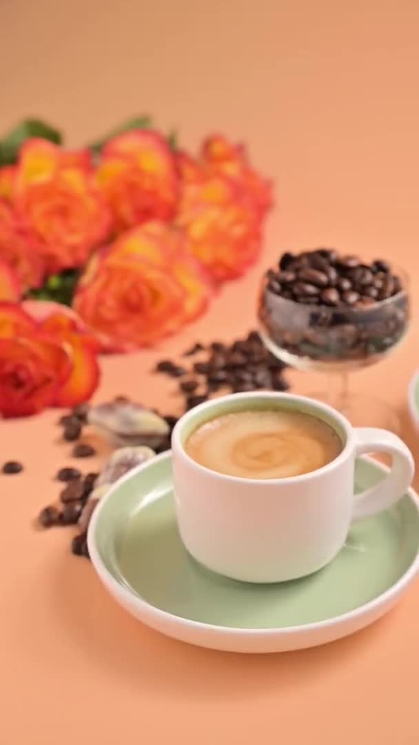 Kawa espresso w ręku. Aromatyczna włoska kawa z piękną śmietaną. Arabica ziarna kawy do produkcji tradycyjnego napoju i bukiet róż na tle. Pionowe wideo. — Wideo stockowe