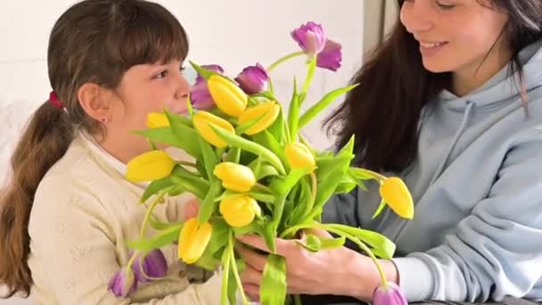 Маленькая девочка дарит своей матери букет желтых и фиолетовых тюльпанов. Ласковые любящие объятия дочери и мамы в День матери. Подарок на 8 марта для мамы. — стоковое видео