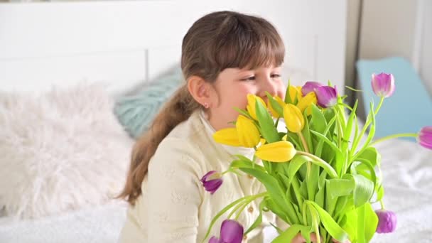 彼女の手に明るいチューリップの花束を持つ小さな女の子、彼女はそれらを嗅ぎ、笑顔。女性の日に母親や祖母への贈り物。3月8日女性の日のコンセプト. — ストック動画