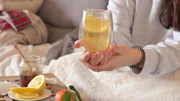 La chica está enferma, se acuesta en la cama y bebe té con limón. Hay pastillas y servilletas en la mesa. Tratamiento del coronavirus durante una pandemia. Concepto de salud. — Vídeo de stock