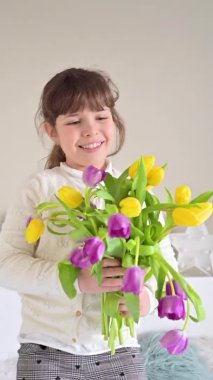 Elinde parlak lalelerden oluşan bir buket olan küçük bir kız, 8 Mart 'ta ya da Anneler Günü' nde bunları annesine veriyor. Annem ya da büyükannem için bir hediye. Bahar çiçeği buketi. Dikey 