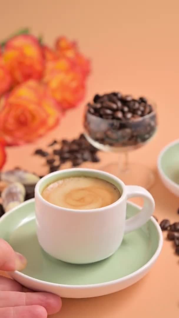 Una piccola tazza di caffè espresso con schiuma e chicchi di caffè spruzzati su uno sfondo luminoso. Pausa caffè con una bevanda tradizionale italiana. Video verticale. Per i social network. — Video Stock