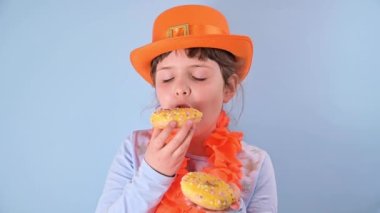 Hollanda 'da Krallar Günü. Geleneksel festival 27 Nisan 'da Hollanda' da gerçekleşti. Mavi arka planda turuncu şapkalı küçük bir kız renkli çörekler yiyor..