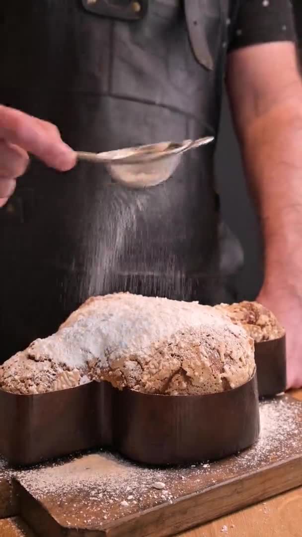 Sobremesas italianas tradicionais de Easter - pomba de Easter. Um homem polvilha açúcar gelado em doces produtos de panificação de férias com amêndoas. Imagens escuras. Movimento lento. Imagens FullHD de alta qualidade. Vista vertical — Vídeo de Stock