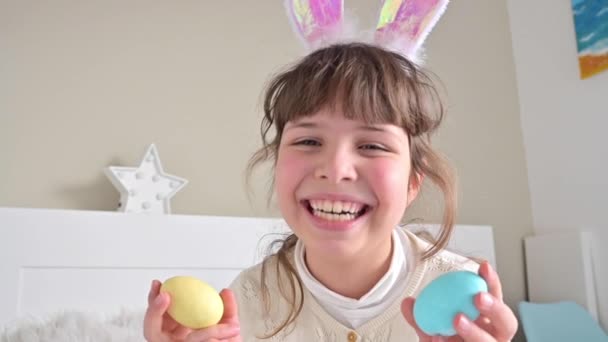 Κοριτσάκι με αυτιά κουνελιού διασκεδάζει και παίζει με πασχαλινά αυγά διαφορετικών χρωμάτων. Διασκέδαση το Πάσχα. — Αρχείο Βίντεο